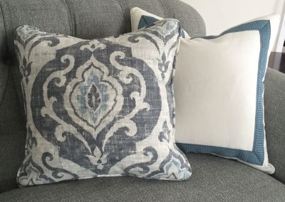 Off white pillow with blue banding, gross grain tape, blue and gray decor, gray sofa, gray couch, living room decor, mitered corners, tufted couch, white walls, needham